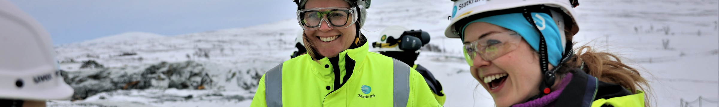 Duas mulheres vestidas de EPIs sorriem em um ambiente externo com neve.